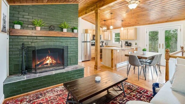 Ein gemütliches Wohnzimmer mit Kamin, Holzboden und einem Essbereich, im Hintergrund eine Küche.