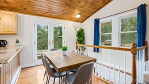 Eine Holzbalkendecke, ein Esstisch mit Stühlen, eine Küchenarbeitsplatte und ein Blick ins Freie durch ein Fenster.