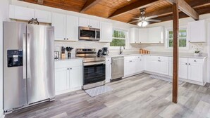 Una cocina moderna con armarios blancos, electrodomésticos de acero inoxidable y techo de madera.