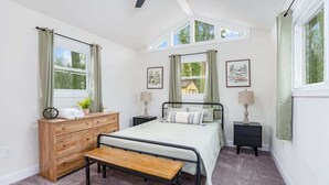 Un dormitorio con cama, cómoda de madera, dos mesitas de noche y un banco.