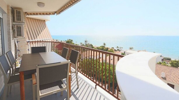 Un balcon avec une table et des chaises, donnant sur une plage et la mer.