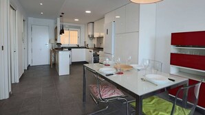 Une cuisine moderne avec des meubles blancs, une table à manger pour quatre personnes et un mur d’accent rouge.