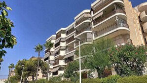Un immeuble résidentiel à plusieurs étages, doté de balcons et entouré de verdure et de palmiers.
