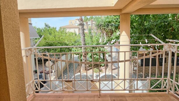 Un balcon avec une balustrade en métal donnant sur une cour intérieure agrémentée de verdure, avec un bâtiment en arrière-plan.
