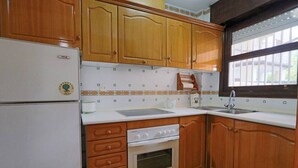 Une cuisine avec des meubles en bois, un réfrigérateur blanc, une cuisinière et une fenêtre avec des stores.