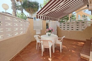 Un patio con una mesa redonda y sillas, cerca blanca y una pérgola.