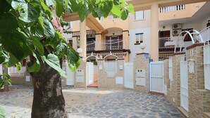 Une cour avec un sol en pierre, un arbre et un bâtiment doté de nombreux balcons et de plusieurs portails.