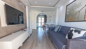 Un salon moderne avec un canapé gris, une console blanche et un grand téléviseur fixé au mur.