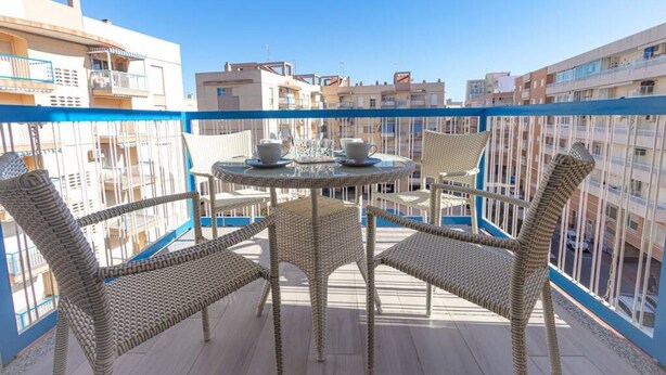 Un balcon doté de meubles en osier et d’une table, offrant une vue sur un paysage urbain avec de nombreux immeubles.