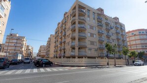 Un immeuble résidentiel à plusieurs étages, doté de balcons, avec un passage piéton et des voitures garées.