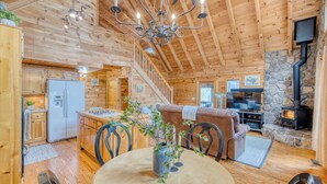 L’intérieur d’un chalet en bois comprend un coin repas, une cuisine et une cheminée en pierre.