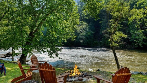 Un terrain de camping situé au bord de la rivière, équipé de chaises en bois et d’un foyer.