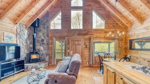 L’intérieur d’une cabane en rondins, avec une cheminée en pierre, un plafond en bois et de grandes fenêtres.