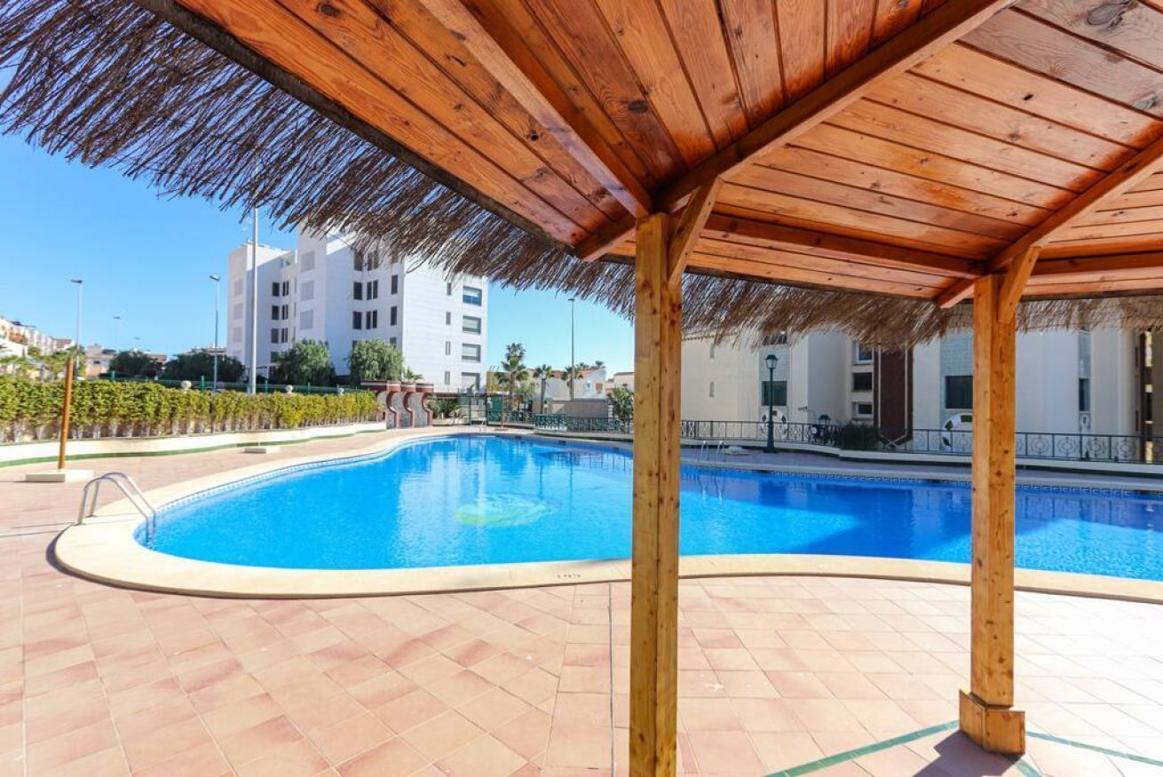 Een zwembad met een houten pergola en een betegeld zonnedek.