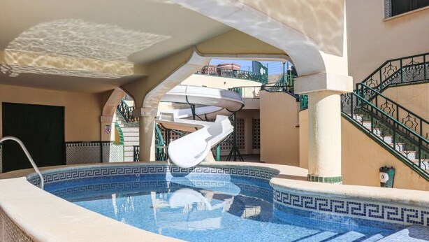 Une piscine dont le carrelage présente un motif géométrique, un fauteuil de relaxation blanc et un escalier en colimaçon.