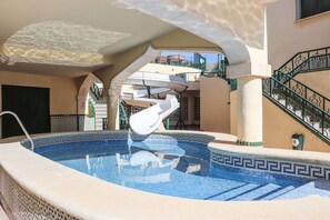 A swimming pool with a geometric tile design, a white lounge chair, and a spiral staircase.