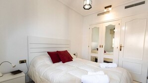 Un lit bien fait, avec une literie blanche et des oreillers rouges, une table de chevet avec une lampe et une armoire avec un miroir.