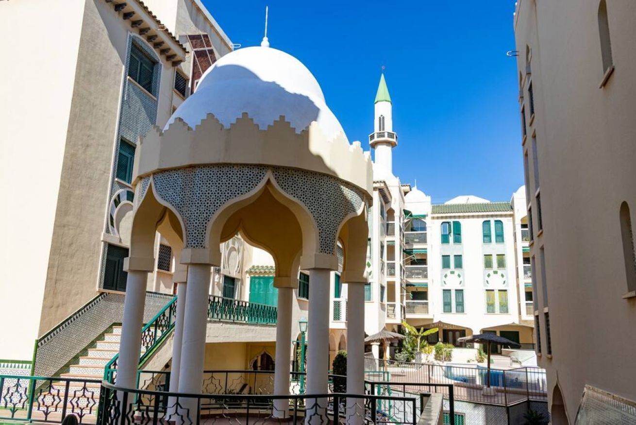 Une cour intérieure avec un pavillon central, une piscine et une mosquée en arrière-plan.