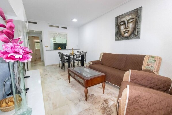 A living room with a brown sofa, a glass coffee table, and a dining area with a table and chairs.