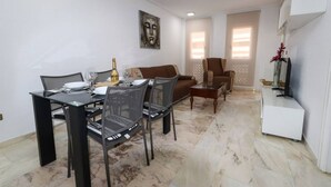 Un coin repas avec une table dressée pour deux personnes, un canapé et un téléviseur posé sur un meuble.