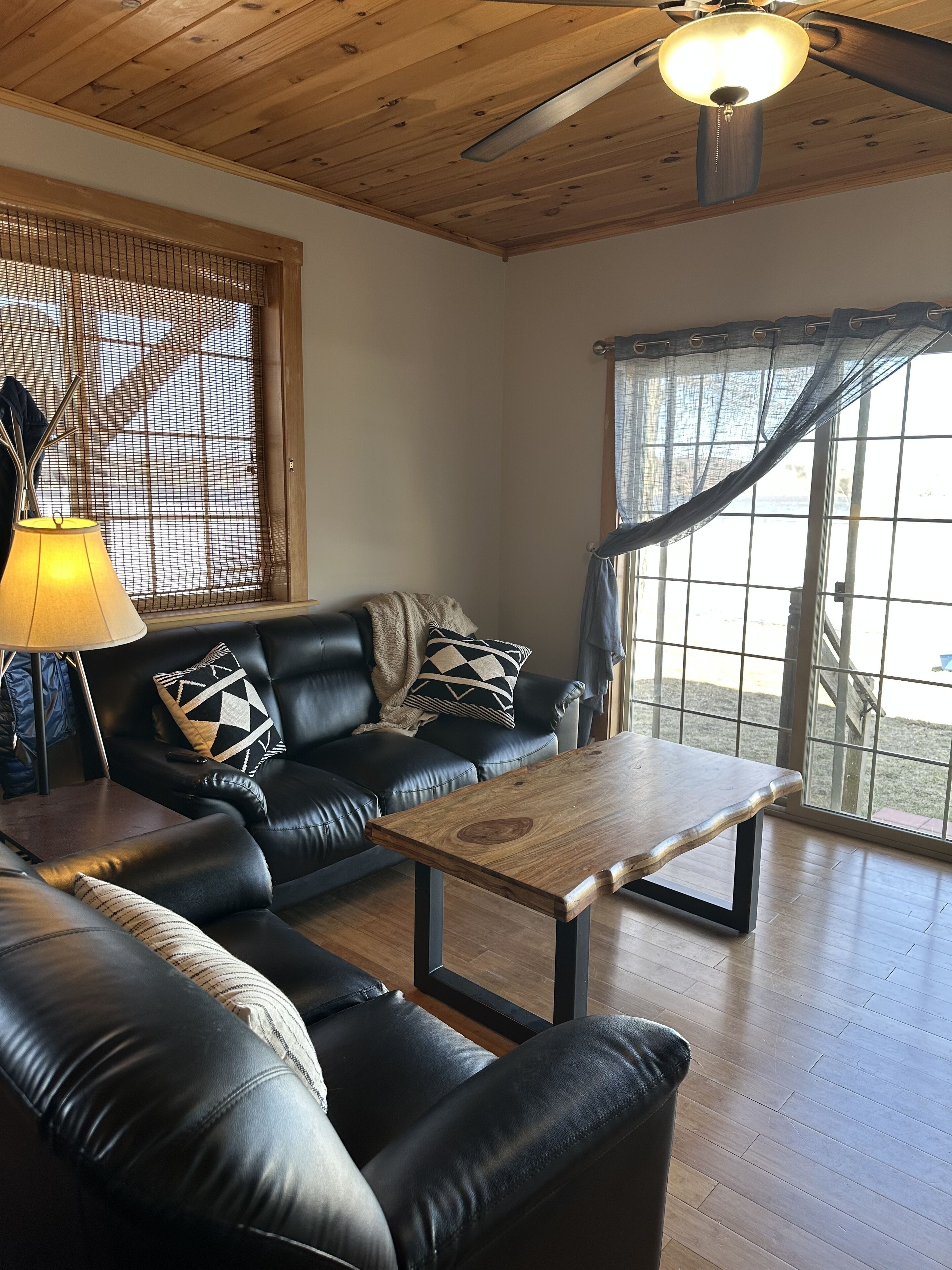 A living room with a black leather sofa, a wooden coffee table, and a ceiling fan.