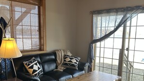 A living room with a black leather sofa, a wooden coffee table, and a ceiling fan. - Lakefront All Season Home (Sabattus)