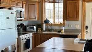 A kitchen with wooden cabinets, a white refrigerator, a stove, a microwave, and a sink. - Lakefront All Season Home (Sabattus)