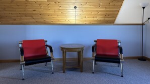 A room with a sloped ceiling, two red chairs, a small wooden table, and a floor lamp. - Lakefront All Season Home (Sabattus)