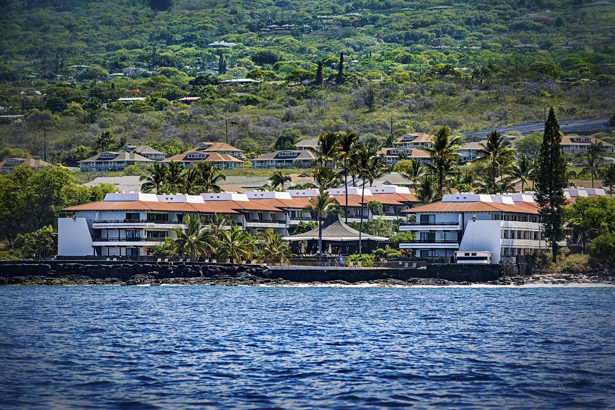 A coastal hotel with multiple buildings, a beachfront, and lush greenery in the background.