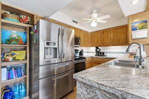 A kitchen with wooden cabinets, a stainless steel refrigerator, a microwave, and a granite countertop.