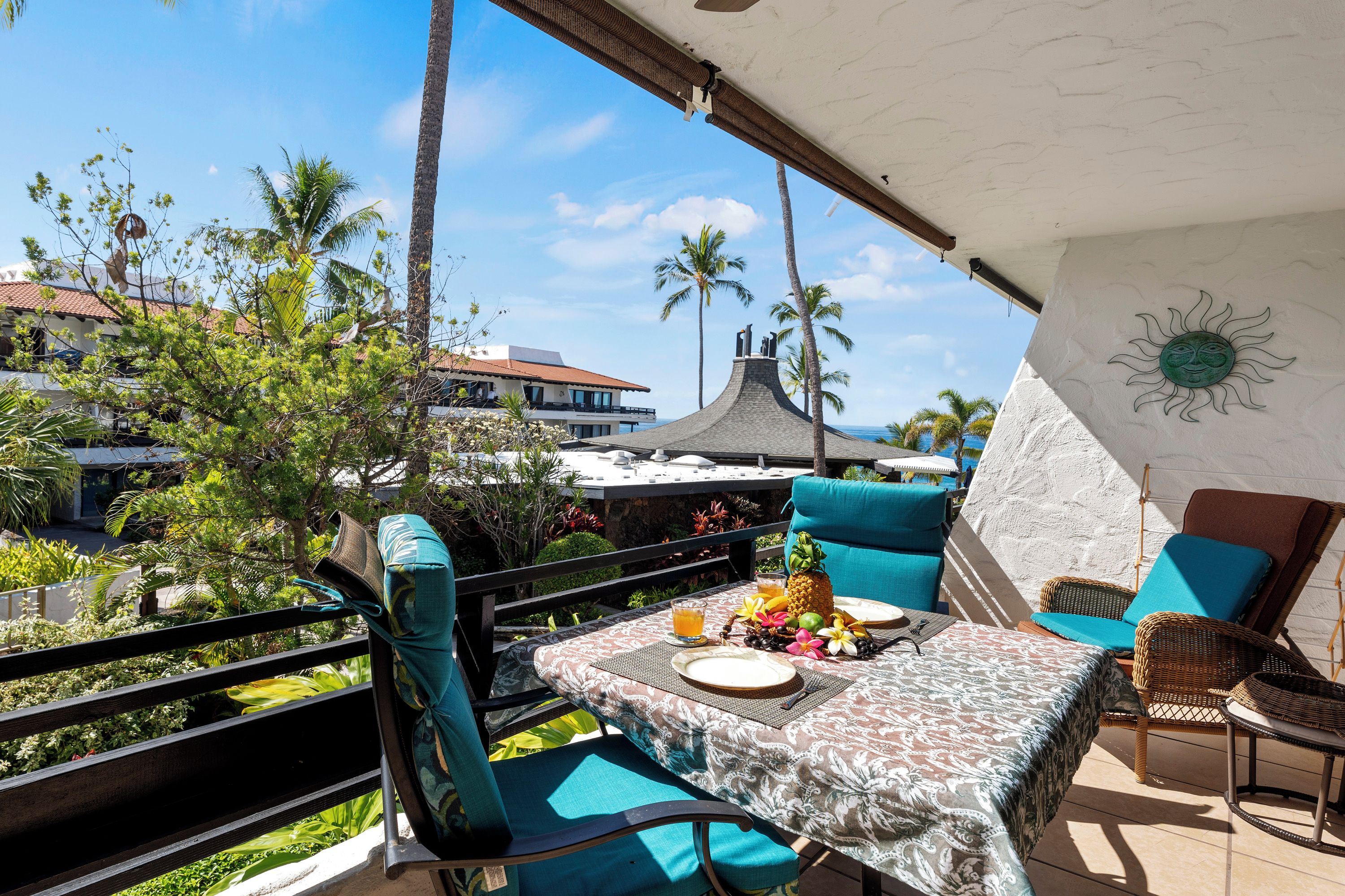 A balcony with a table set for two, chairs, and a view of palm trees and buildings.