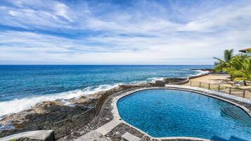 A circular pool with a stone border, adjacent to a rocky shoreline and a beach.