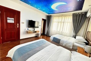 A hotel room with two beds, a television, a desk, and a ceiling mural of a starry sky with a crescent moon.