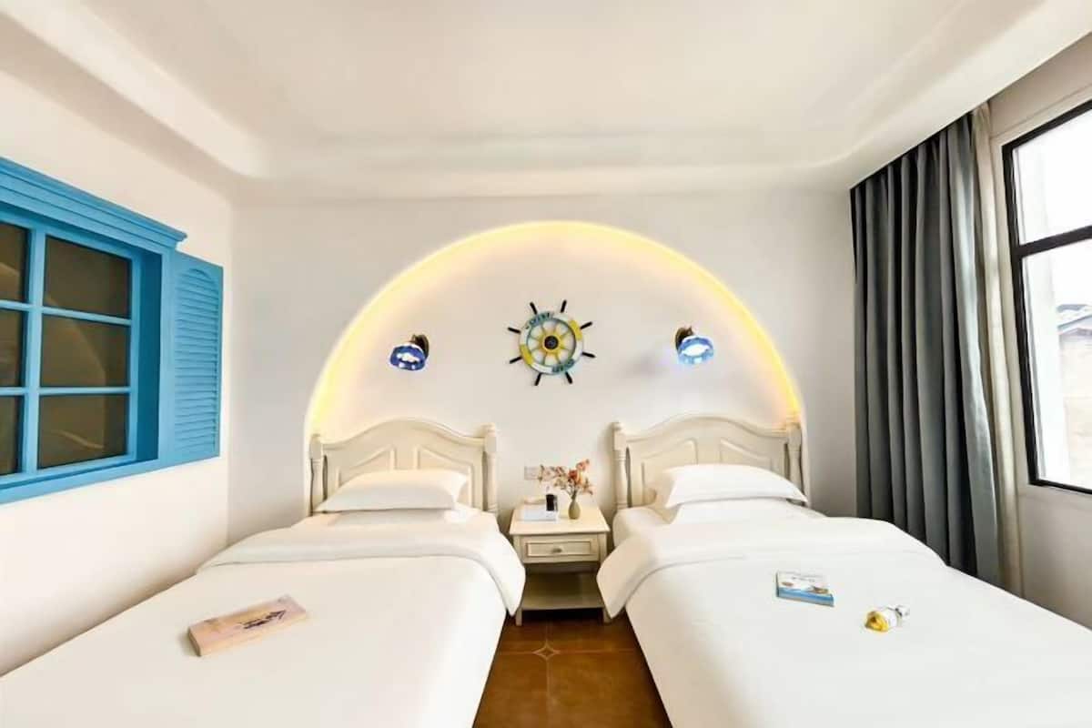 A hotel room with two beds, a small table with a vase, and a wall clock.