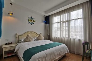 A neatly made bed with a white and teal bedspread, a wooden headboard, and a wall clock. There is a nightstand with a lamp and a small table beside the bed. A window with sheer curtains allows natural light into the room. - No. 1 Inn @ the Corner (Zhangjiajie)