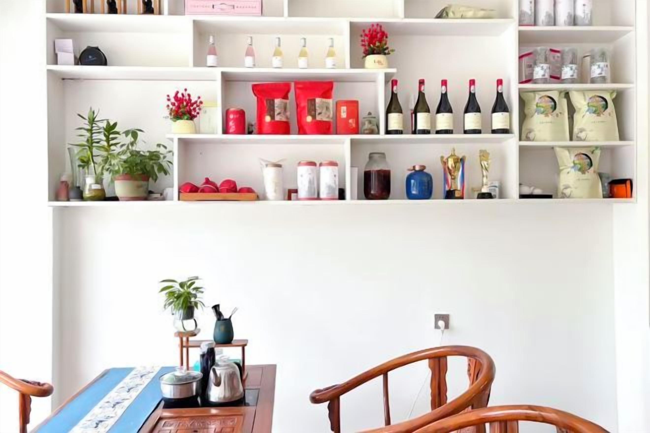 A dining area with a wooden table, chairs, and a variety of items on shelves above, including wine bottles and decorative objects.