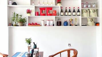A dining area with a wooden table, chairs, and a variety of items on shelves above, including wine bottles and decorative objects.