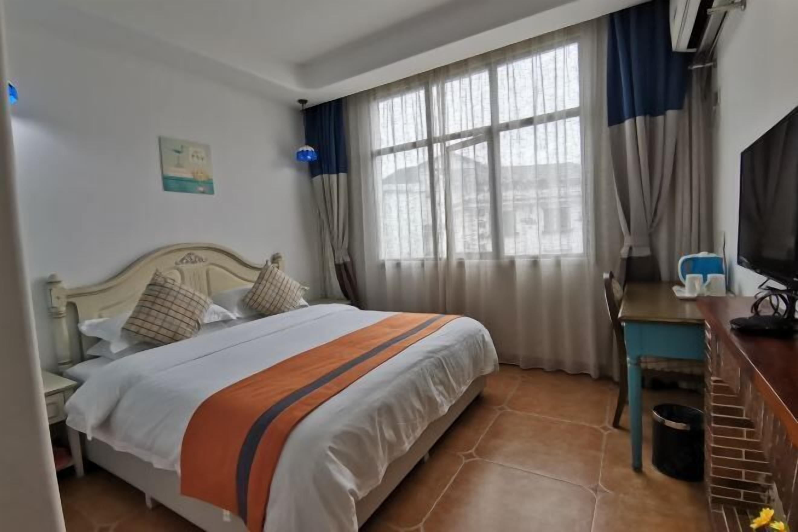 Una habitación de hotel con cama, escritorio, televisión y ventana con cortinas.