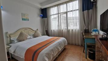 Una habitación de hotel con cama, escritorio, televisión y ventana con cortinas.