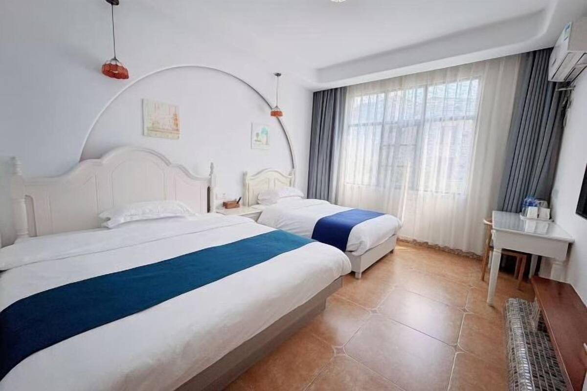 A hotel room with two beds, a desk, and a window with curtains.