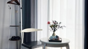 A room with a chair, a small table with a vase of flowers, and a shoe rack with shoes and a hanger. - No. 1 Inn @ the Corner (Zhangjiajie)
