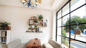 A room with a large window, a wooden table, two patterned sofas, and shelves with books and plants. - No. 1 Inn @ the Corner (Zhangjiajie)