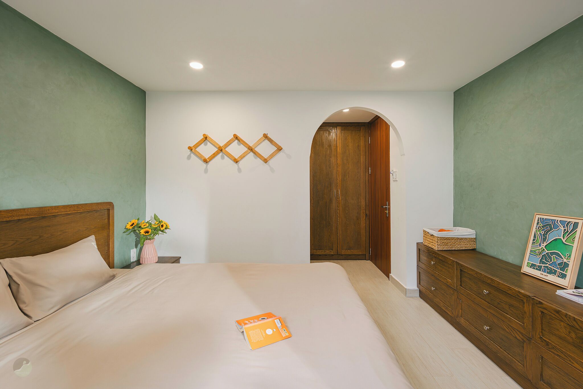 A bedroom with a bed, wooden wardrobe, and a wall-mounted shelf with a framed map.