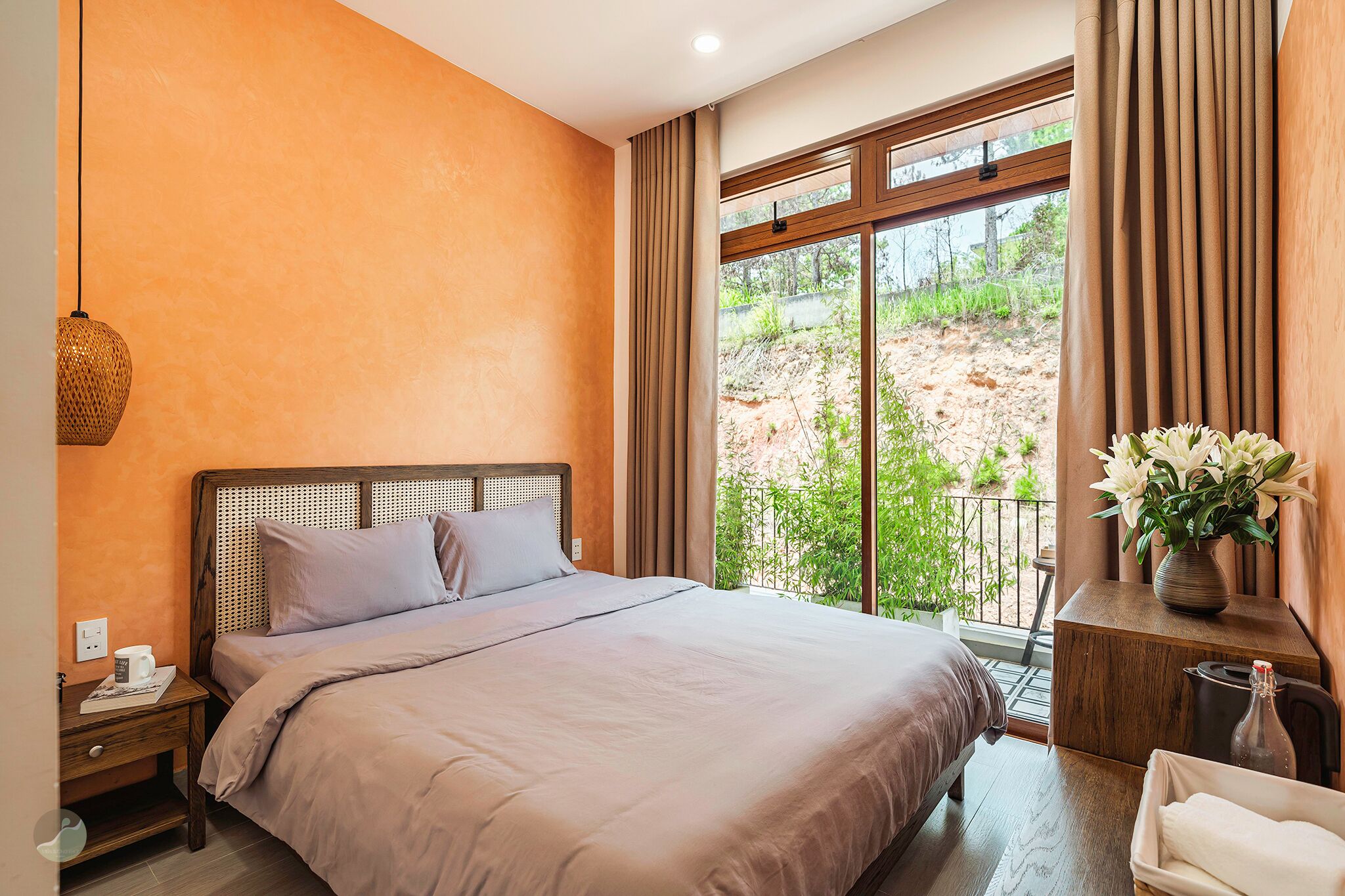 A bedroom with a large bed, a nightstand, a bedside table, a window with curtains, and a potted plant.