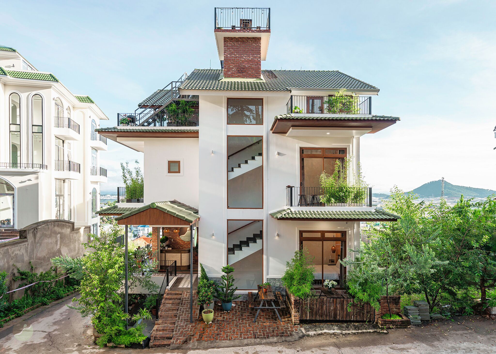 A multi-story building with a central staircase, balconies, and a garden area with potted plants.