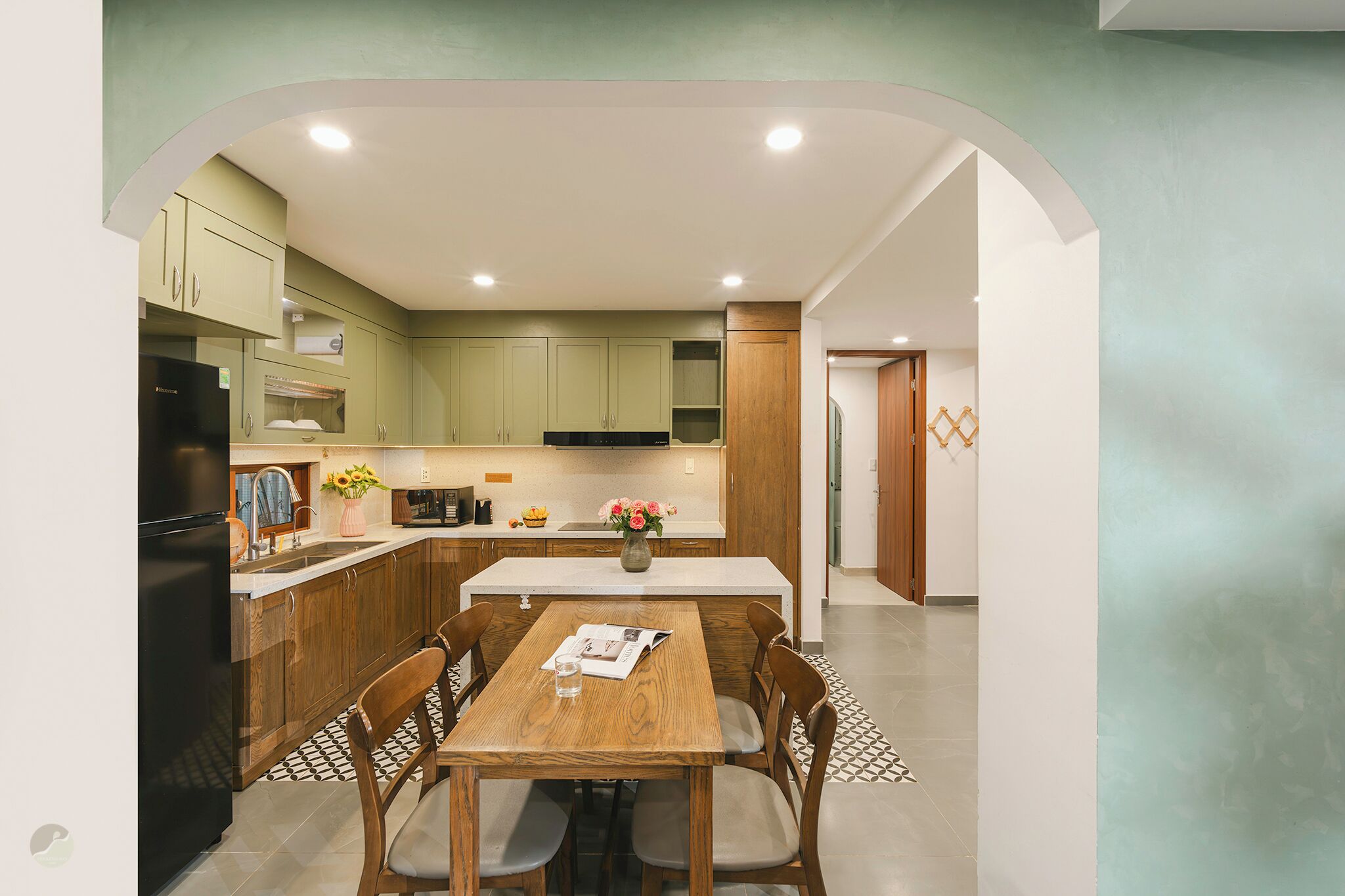 Una cocina moderna con armarios de madera, un refrigerador negro y una zona de comedor con mesa y sillas de madera.