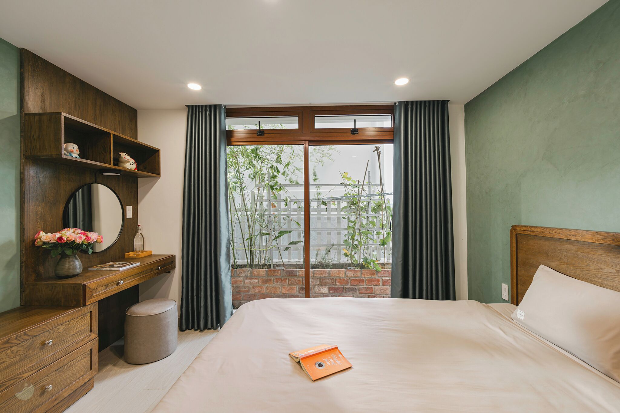 A bedroom with a bed, a wooden dresser, a mirror, and a window with curtains.