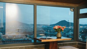A room with a large window, a wooden table with a vase of flowers, and a book. - Mien Suong Khoi - Home & Cafe (Xuan Truong - Da Lat)