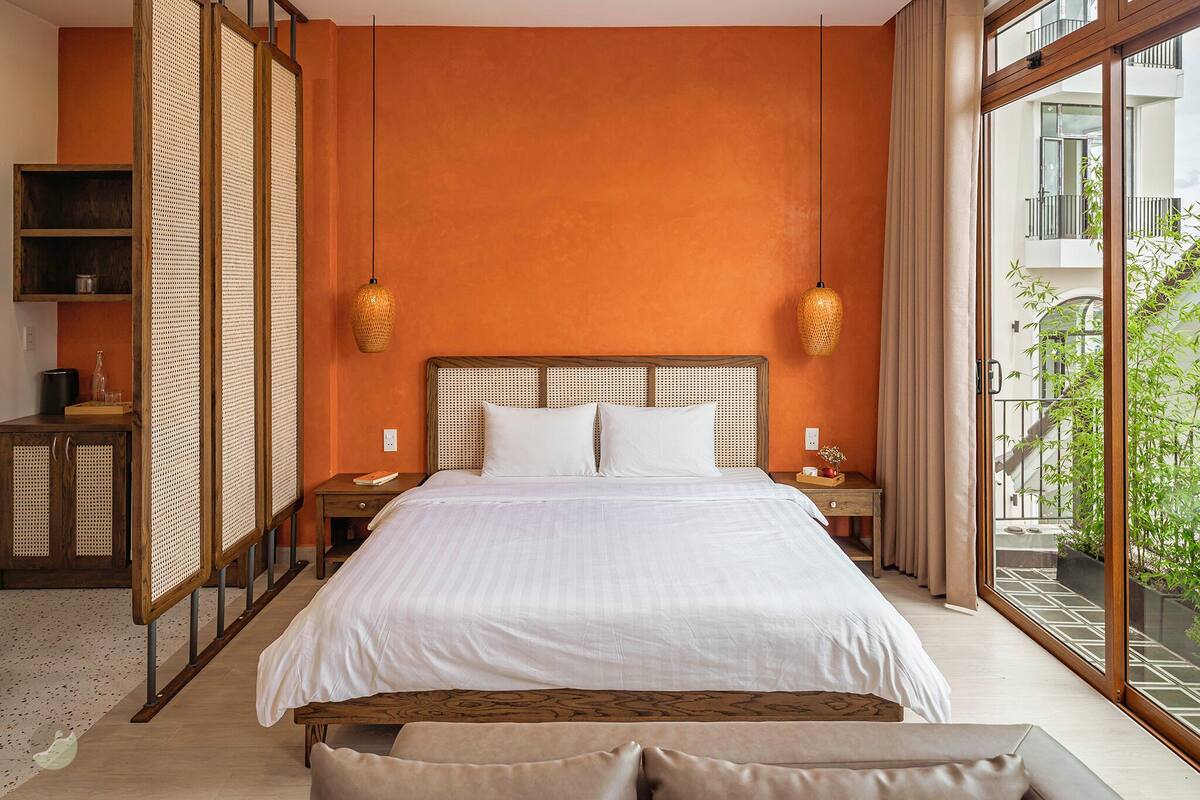A bedroom with a large bed, wooden headboard, two bedside tables, and a view of a balcony with plants.