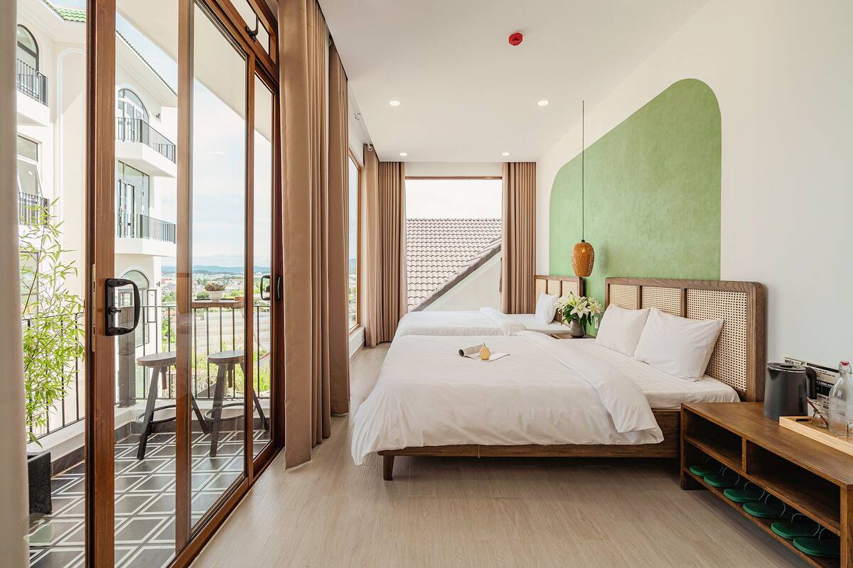 A hotel room with a balcony, a bed, a bedside table, and a view of the city.